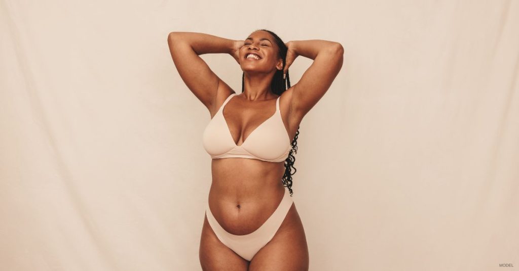 A woman in beige bra and underwear smiling confidently. (Model)